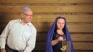 Yahudi aile kocası ve karısı festival masasının yanında bir kadın mum yakıyor bir erkek de çocuk için bir bardak tutuyor..