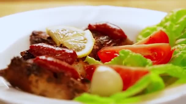 Biała płyta z kawałkami mięsa grillowanego na liściach sałaty z ketchupem i cytryną obraca się w kole — Wideo stockowe