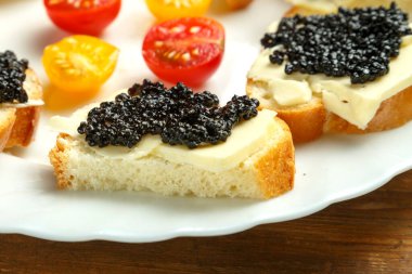 Tahta bir masada kırmızı havyarlı sandviçli beyaz tabak..