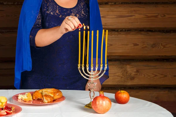 Безликая еврейка в синем плаще зажигает свечи накануне Рош ха-Шана в подсвечнике. — стоковое фото