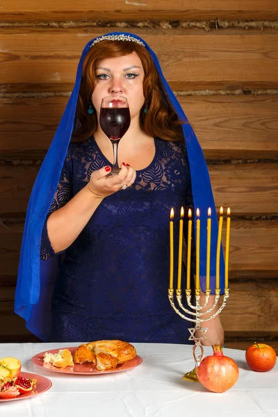 Na véspera de Rosh Ashan, uma mulher judia está ao lado de velas acesas com um copo de vinho Kiddush na mão. — Fotografia de Stock