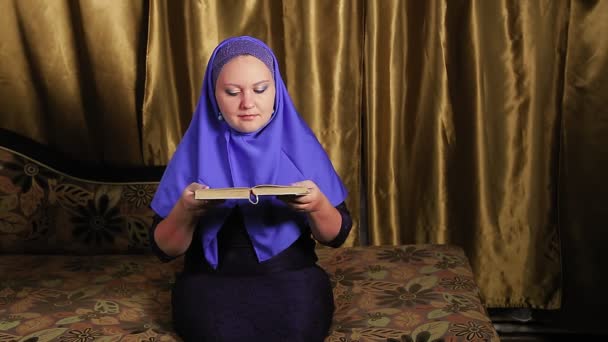 Une jeune femme musulmane dans un hijab bleu lit le livre sacré à la maison — Video