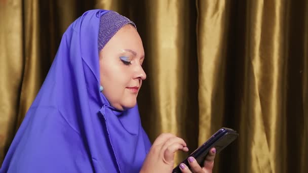 Una joven musulmana en un hiyab azul de perfil charlando en mensajeros en un smartphone. — Vídeo de stock