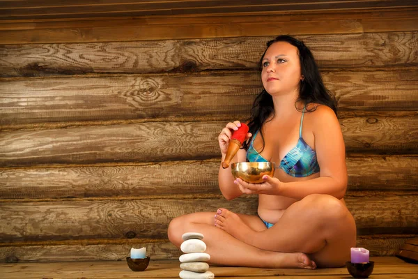 Ung brunett kvinna sitter i ett spa med meditater med en sjungande skål. — Stockfoto