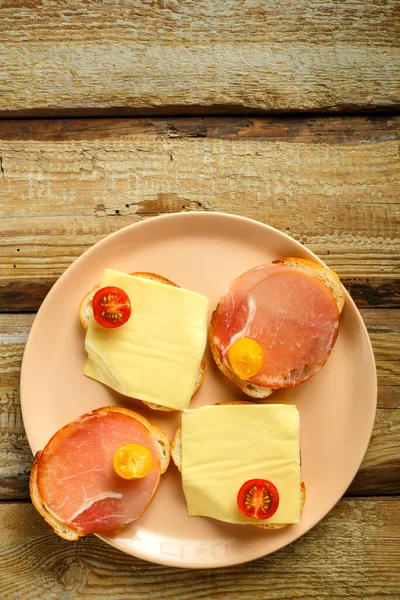 Sanduíches com presunto e queijo e cereja em uma chapa em uma mesa de madeira. Copiar o lugar. — Fotografia de Stock