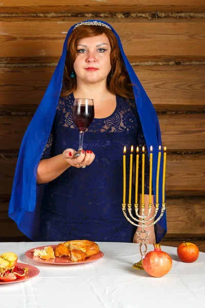 On the eve of Rosh Ashan, a Jewish woman stands next to burning candles with a glass of Kiddush wine in her hand. — Stock Photo, Image