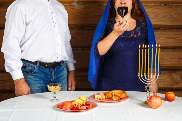 유대인 가족의 남편과 아내가 촛불을 켜고 축제 식탁에 앉아 있다. 납치하기 위해 포도주를 마시는 여자. — 스톡 사진