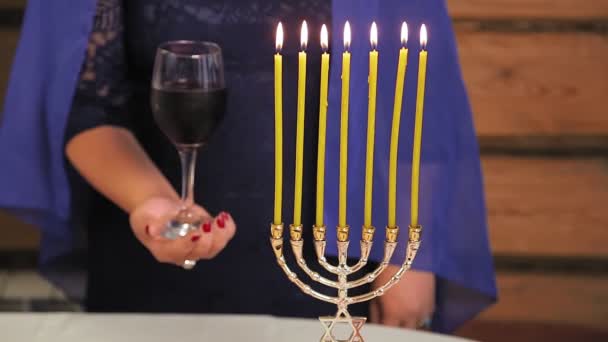 Еврейская женщина без лиц держит стакан Киддуша рядом с горящими свечами — стоковое видео