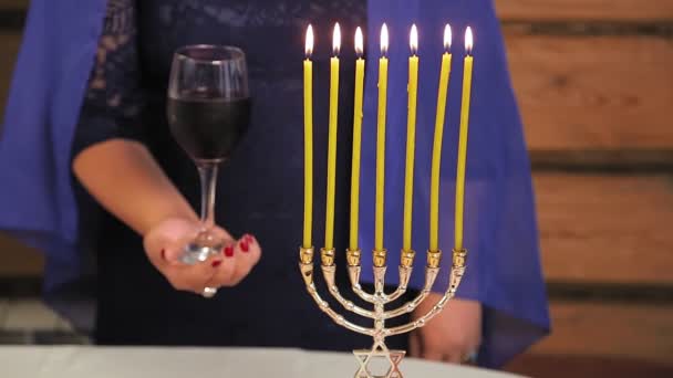 A Jewish woman without faces holds a Kiddush glass next to burning candles — Stock Video