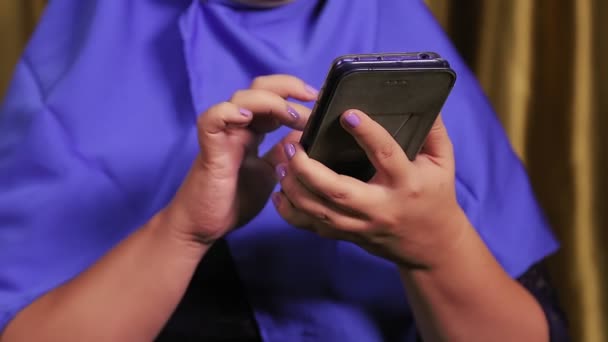 En ung muslimsk kvinde i en blå hijab uden et ansigt, der kommunikerer i instant messengers på en smartphone. – Stock-video