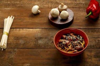 Tay soslu sebze ve mantarlı Udon. Malzemelerin yanında kil tabakta..