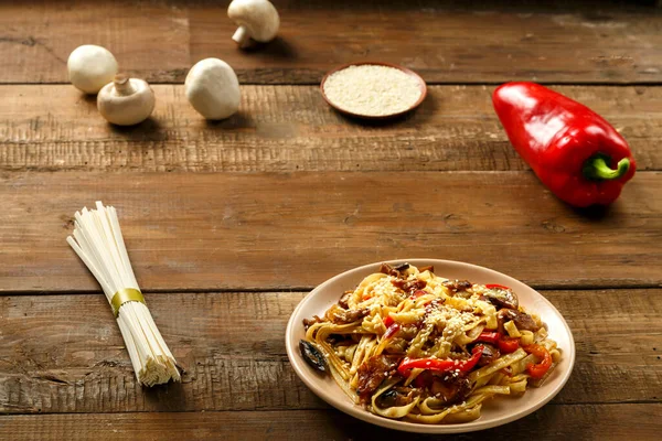 Tayland soslu tavuk ve mantarlı Udon, malzemelerin yanında bej bir tabakta..