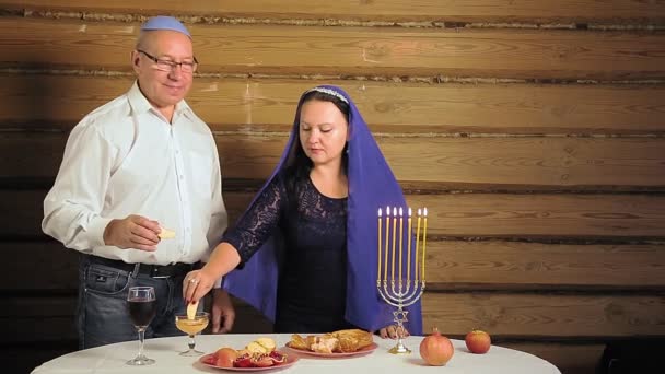 Suami dan istri keluarga Yahudi di dekat meja pesta dengan lilin mencelupkan apel ke dalam madu dan memakannya. — Stok Video