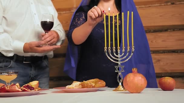Безликая еврейская семья рядом с праздничным столом Рош Ха-Шана женщина зажигает свечи мужчина держит стакан для малыша — стоковое видео