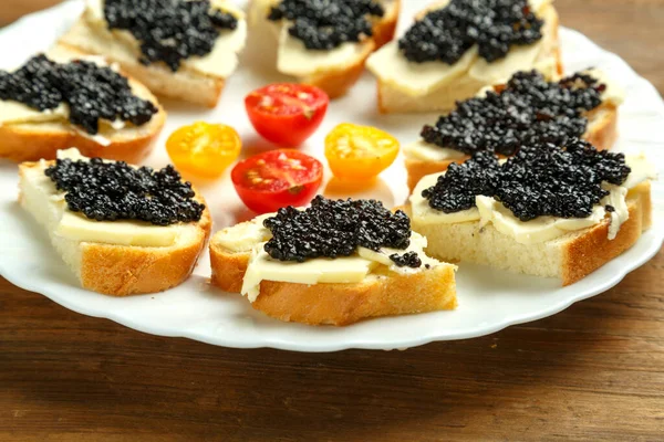 Sandwichs au caviar noir sur une assiette blanche sur une table en bois. — Photo