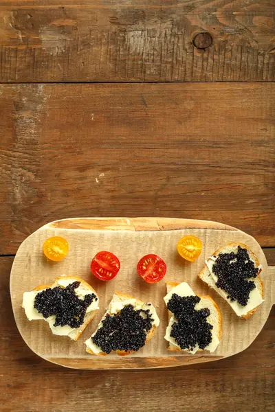 Sanduíches com caviar preto em uma tábua de madeira em uma mesa de madeira, lugar de cópia. — Fotografia de Stock