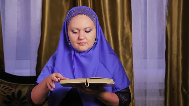 Een jonge moslimvrouw in een blauwe hijab leest het heilige boek — Stockvideo
