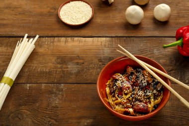 Tay soslu sebze ve mantarlı Udon. Yanında yemek çubukları olan kilden bir tabakta..