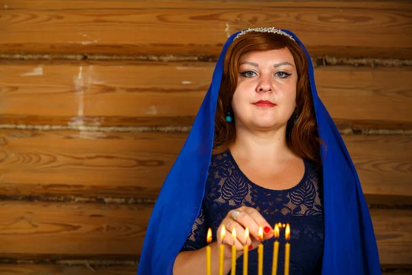 Молодая еврейская жена в синем плаще на голове зажигает свечи накануне Рош ха-Шана в подсвечнике. — стоковое фото