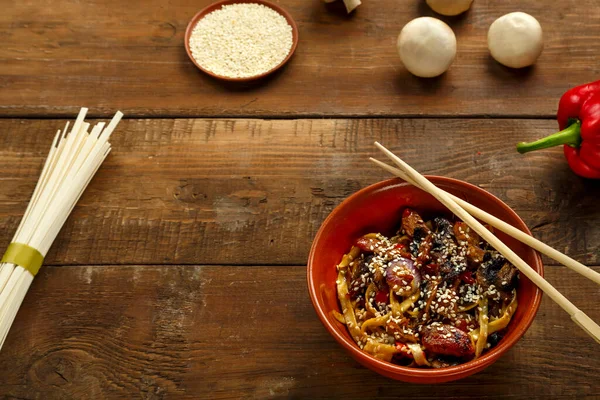 Tay soslu sebze ve mantarlı Udon. Yanında yemek çubukları olan kilden bir tabakta..