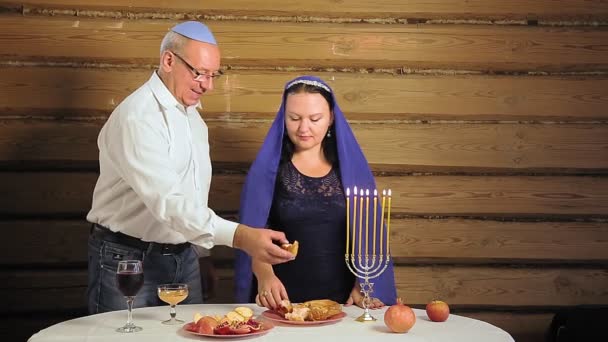 Een Joods gezin, een man en vrouw bij de feestelijke tafel en kaarsen, dompel challah in honing en eet — Stockvideo