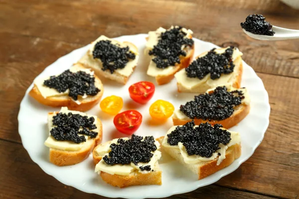 Assiette blanche avec sandwichs au caviar rouge sur une table en bois. — Photo