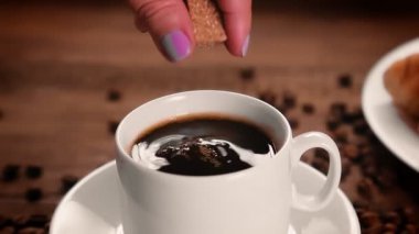 Bir kadın eli, kahverengi şekeri kahve bardağına koyar..