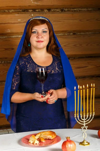 Na véspera de Rosh Ashana, uma mulher judia está em uma mesa festiva com velas acesas com um copo de vinho kiddush em sua mão. — Fotografia de Stock