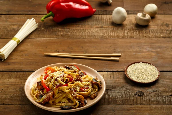 Tayland soslu tavuk ve mantarlı Udon, malzemelerin yanında bej bir tabakta..