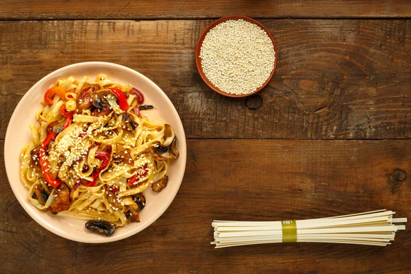 Tayland soslu tavuk ve mantarlı Udon susam ve udonun yanında bej bir tabakta..