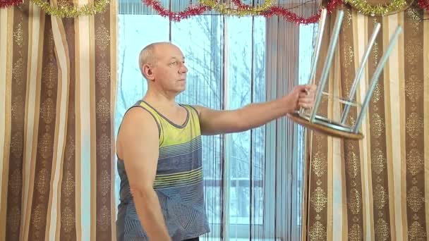 Un homme en formation à la maison avec secoue les muscles avec des selles au lieu d'un haltère. — Video