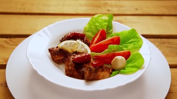 O placă albă cu bucăți de carne la grătar pe frunzele de salată se rotește într-un cerc . — Videoclip de stoc