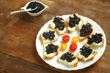 Tahta bir masada, siyah havyarlı sandviçler bir kaşıkla havyar tabağının yanında. Yatay fotoğraf