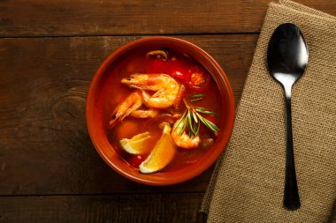 Tom yer elması çorbası, karides ve limonlu, kahverengi bir tabakta, tahta bir masada, peçetedeki kaşığın yanında. Yatay fotoğraf