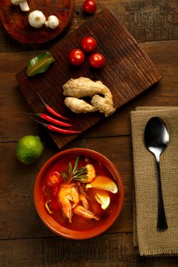 Tom yer elması çorbası, karides ve limonlu, kahverengi bir tabakta, tahta bir masada, peçetedeki kaşığın yanında ve limonlu zencefil karışımı. Dikey fotoğraf