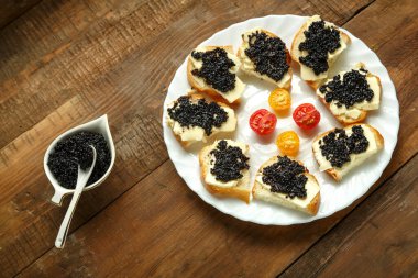 Siyah havyarlı sandviçler, beyaz bir tabakta, tahta bir masada, havyar tabağının yanında kaşık ile..