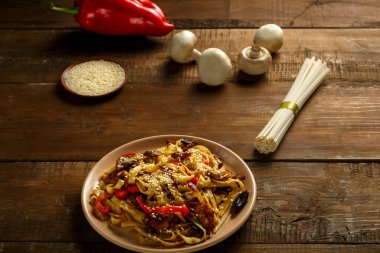 Tay soslu sebze ve mantarlı Udon, malzemelerin yanında bej bir tabakta..