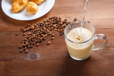 Dağınık kahve çekirdeklerinin arasına bir bardak sıcak su dökülüyor..