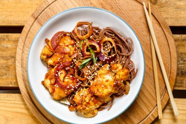 Tavuklu ve susamlı soba tabağı ahşap bir stantta teriyaki soslu ve sopalı..