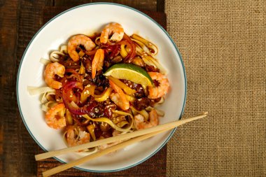 Peçete ve yemek çubuklarının yanında hafif bir tabakta sebzeli, mantarlı ve karidesli udon..