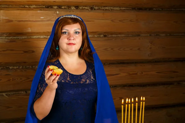 Una joven esposa judía con una capa azul en la cabeza enciende velas en la víspera de Rosh Hashaná en un candelero en forma de menorá. —  Fotos de Stock