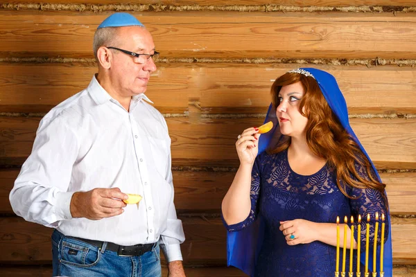 Yahudi bir aile, kippah giymiş bir koca ve Rosh Ashana 'da başlarının üstünde pelerinli bir eş yanan mumlarla yanan bir şenlik masasında bal içinde challah yiyorlar..