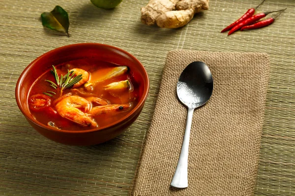 Sopa de ñame Tom con camarones y lima en un plato marrón en una estera de bambú junto a una cuchara en una servilleta e ingredientes jengibre de lima. — Foto de Stock