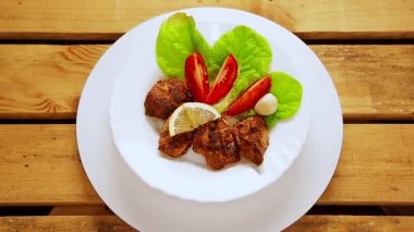 Marul yapraklarının üzerinde ızgara et parçaları olan beyaz bir tabak daire şeklinde döner.