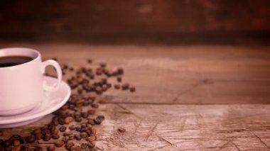 Bir kadın eli masaya bir tabak kruvasanı bir fincan kahve ve kahve çekirdeğinin yanına koyar..