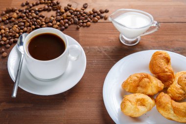 Masada bir fincan kahve şeker ve kremanın yanında bir sürahi ve bir kruvasan..