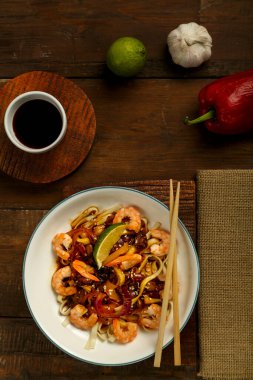 Mantarlı udon ve hafif bir tabakta karides peçete, çubuk ve malzemelerin yanında..