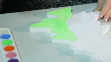 Masadaki odada oturan kadın, yeşil suluboya ile Noel ağacını boyayarak ev için Noel süslemeleri yapıyor.