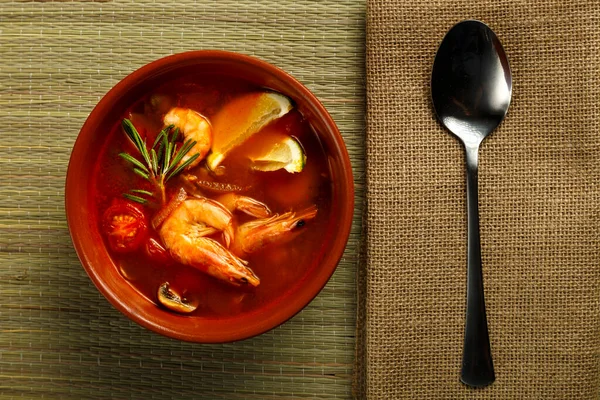 Sopa de ñame Tom con camarones y lima en un plato marrón sobre una mesa de madera junto a una cuchara en una servilleta. —  Fotos de Stock