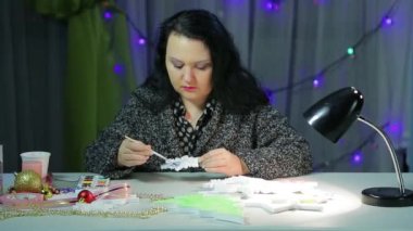 Bir kış akşamında, genç bir kadın Noel için ev dekorasyonu yapar. Mavi suluboya kar taneleri boyayarak..